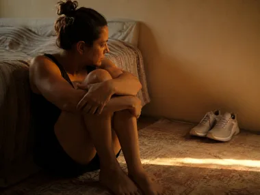 Mulher sentada no chão do quarto ao lado de um par de tênis de treino novo